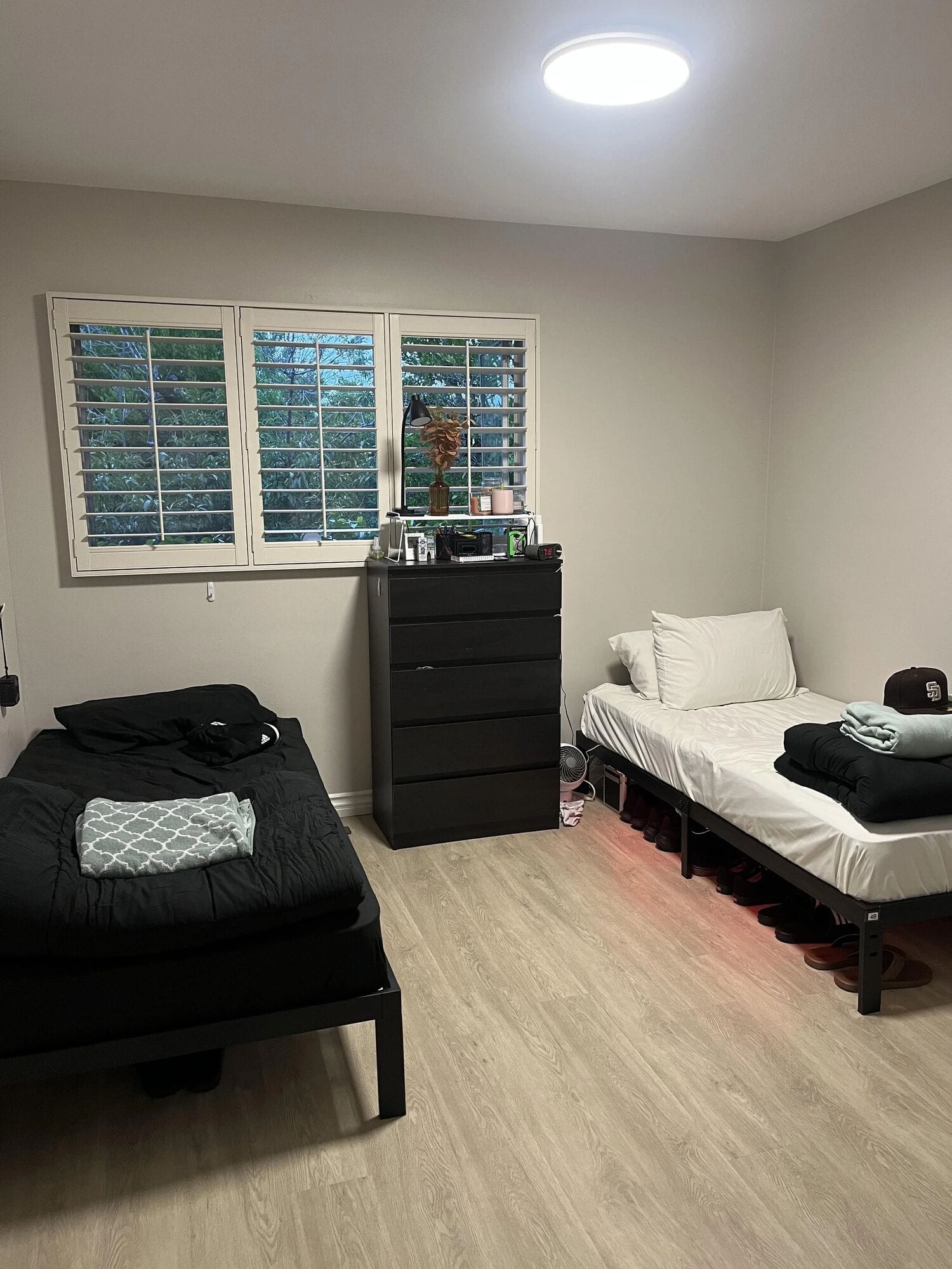 A Clubhouse bedroom with two twin beds, a dark dresser and a shuttered window