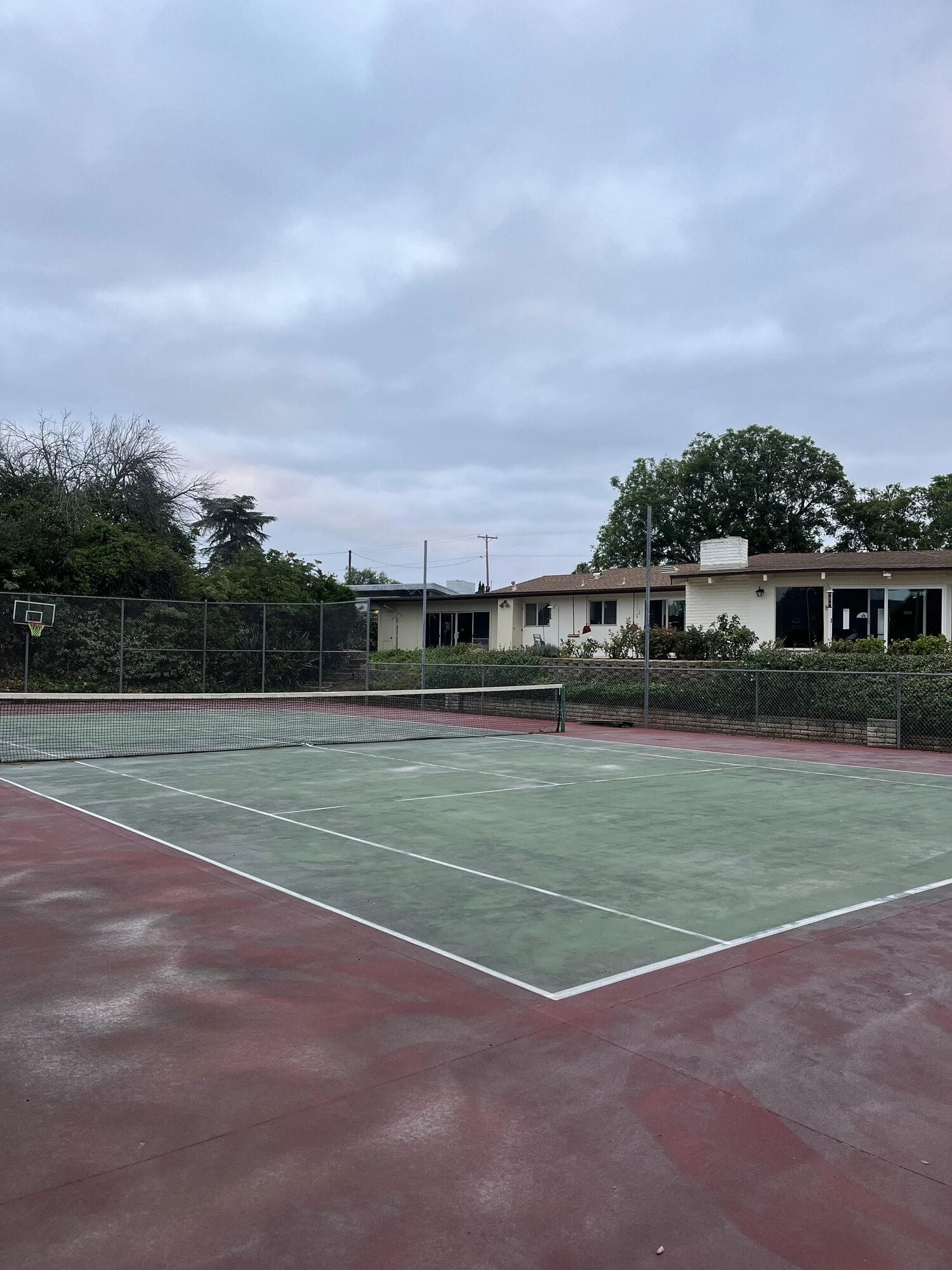 The Clubhouse tennis court, with the house and trees beyond the fence