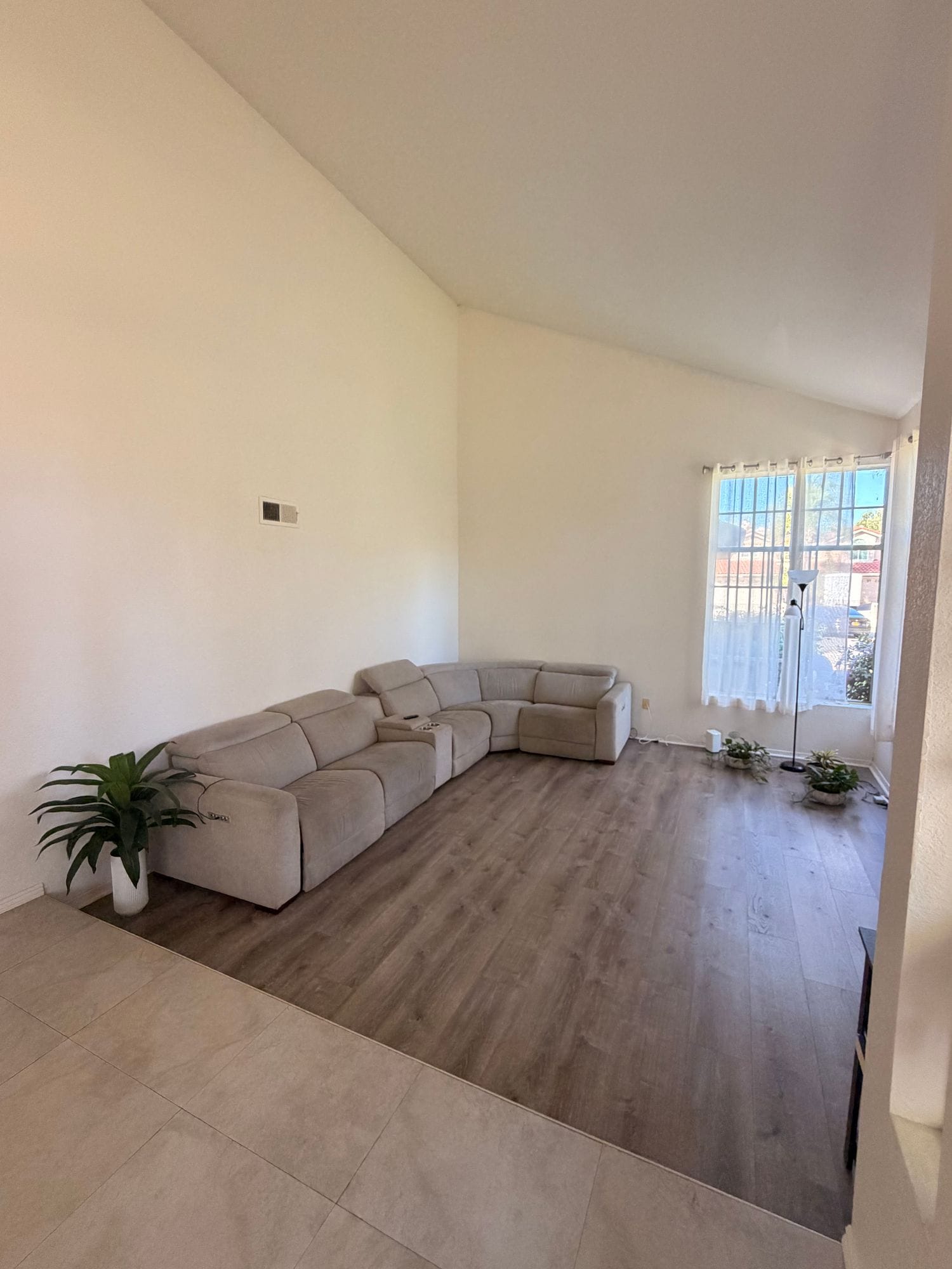 Parkhouse living room with a vaulted ceiling, a large beige sectional and a tall window onto the street