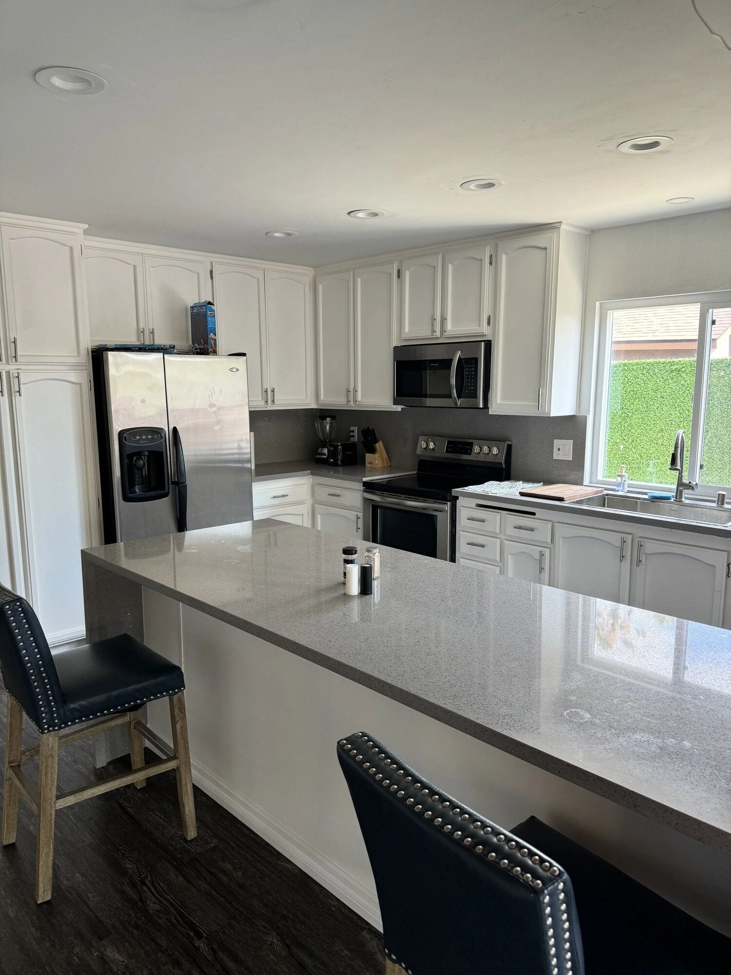 Poolhouse kitchen with a long quartz island, bar stools, white cabinets and a stainless refrigerator