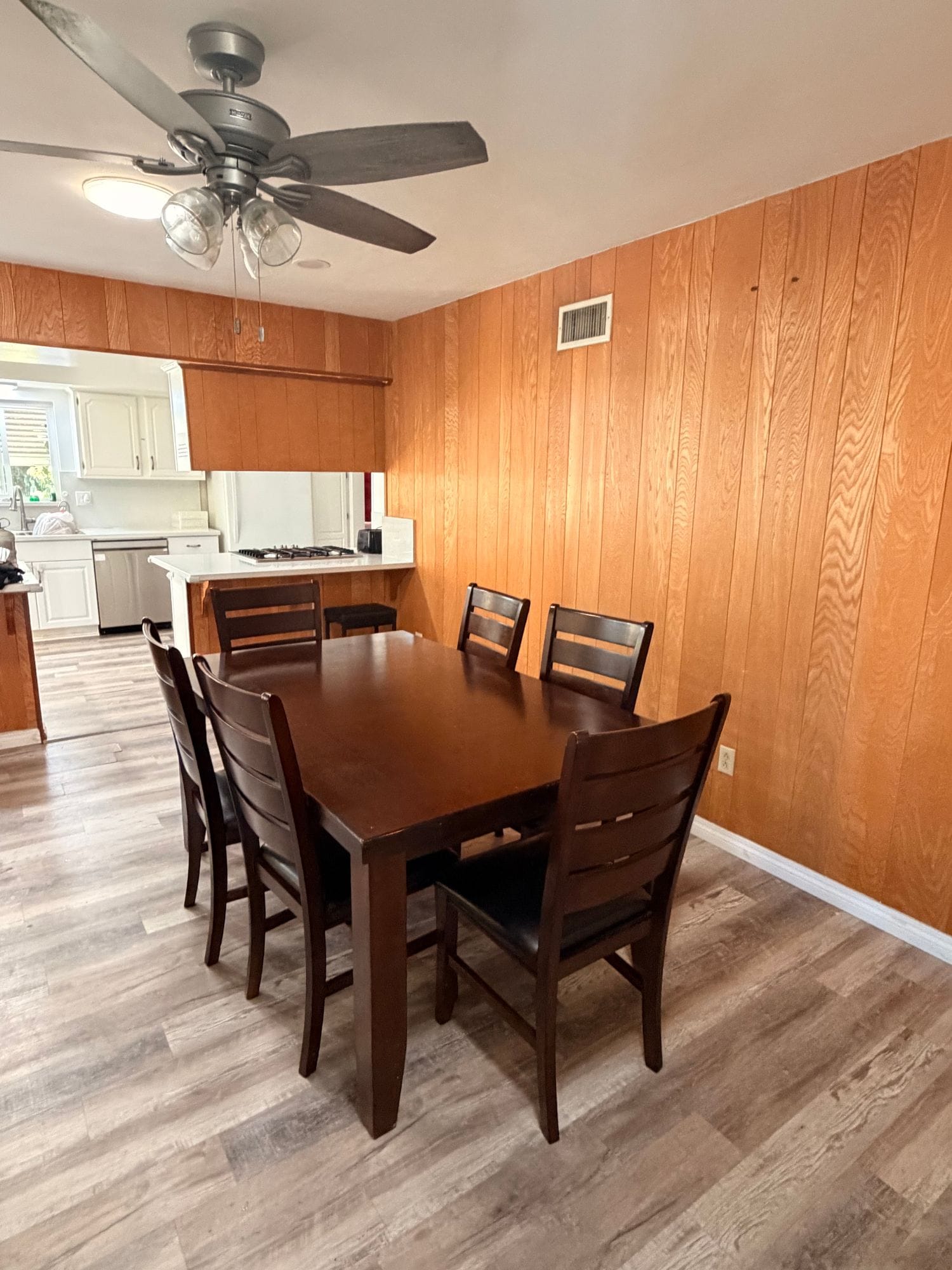 Ranchhouse dining area with a dark wood table for six against wood-paneled walls, opening onto the kitchen