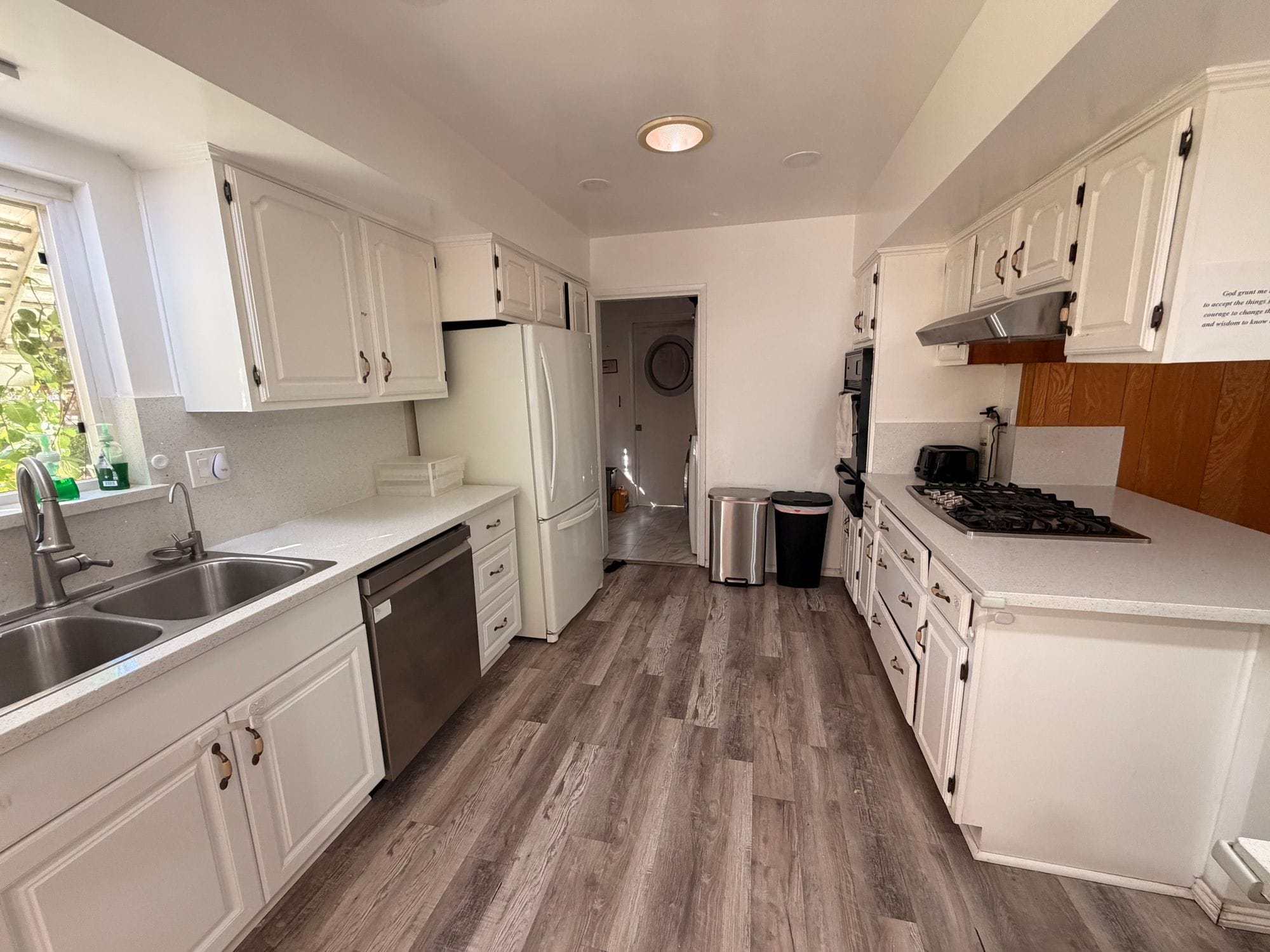 Ranchhouse galley kitchen with white cabinets, a gas cooktop, a stainless dishwasher and wood-look floors